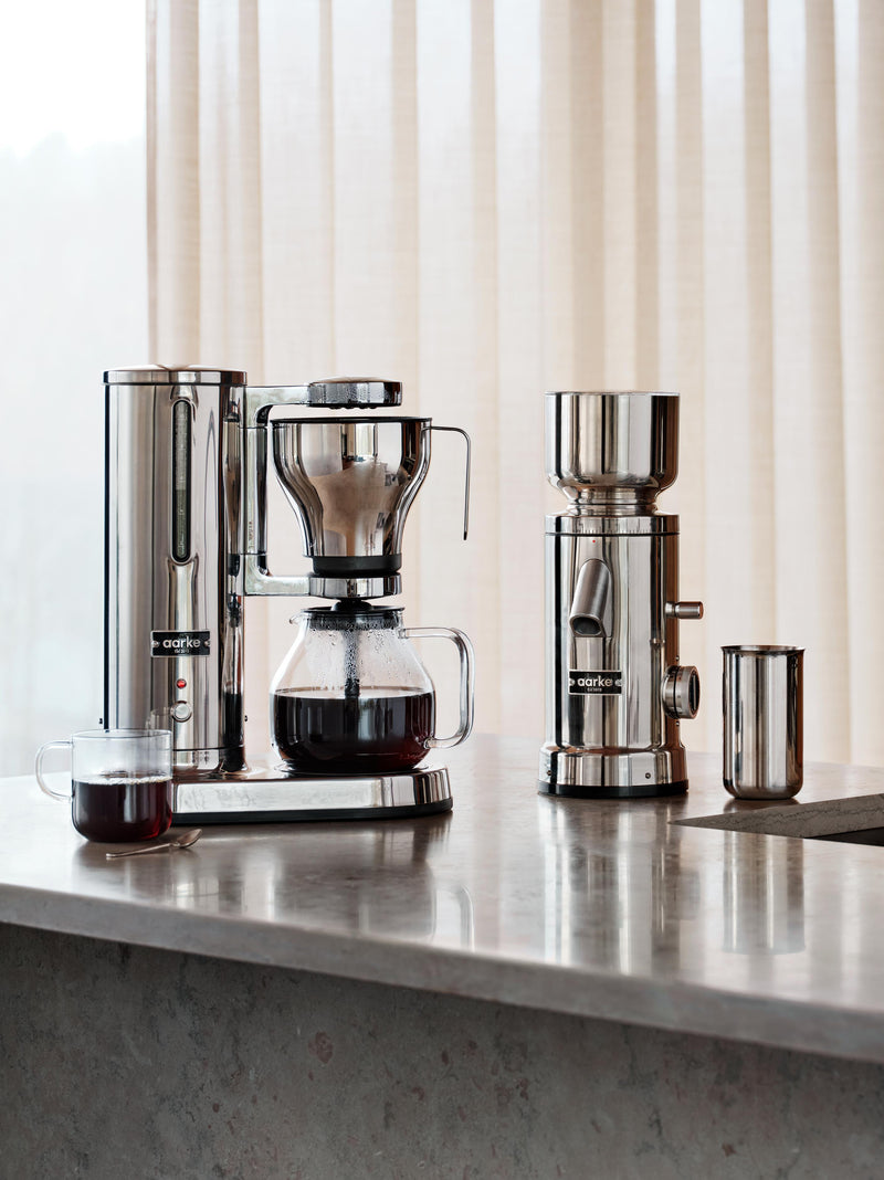 aarke coffee maker and coffee grinder standing on kitchenisland in a setting of marble stone. 