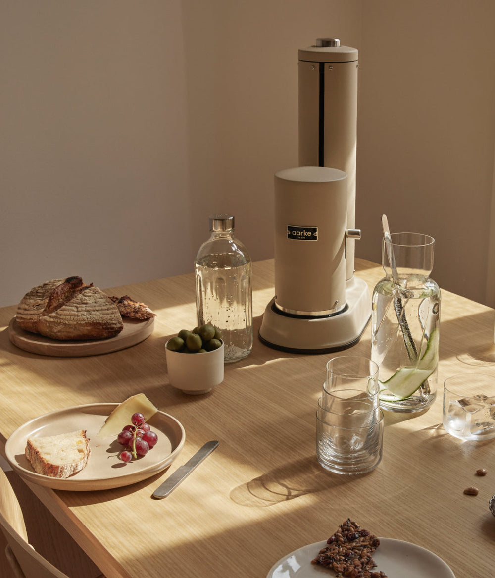 carbonator pro sand standing on the dinner table next to the aarke glass bottle.