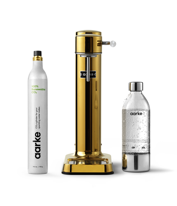 Front view of the Carbonator 3 in Gold beside a PET water bottle and 1 Aarke CO2 Cylinder.